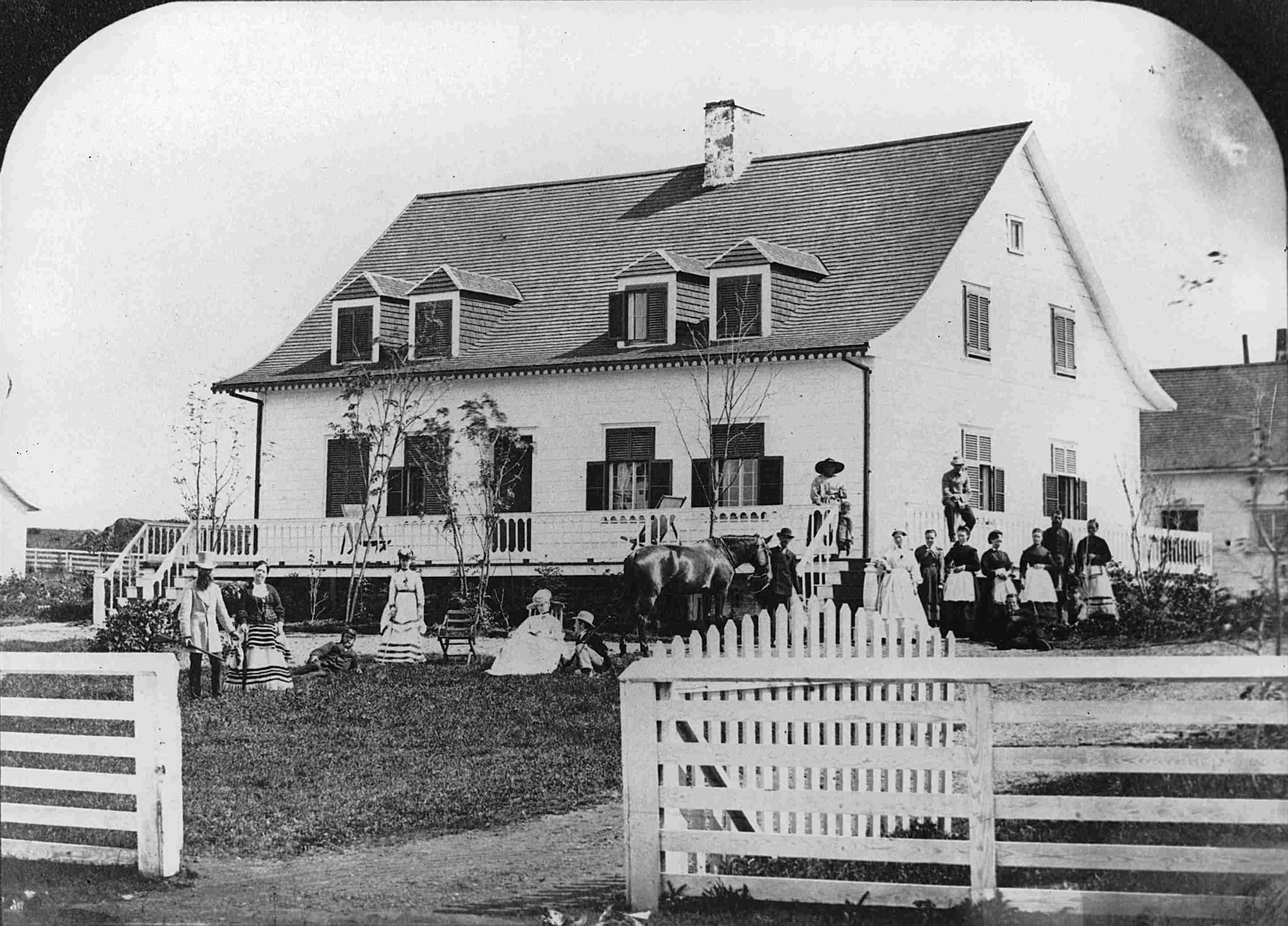 A group of fifteen people posing in front of an old country home.