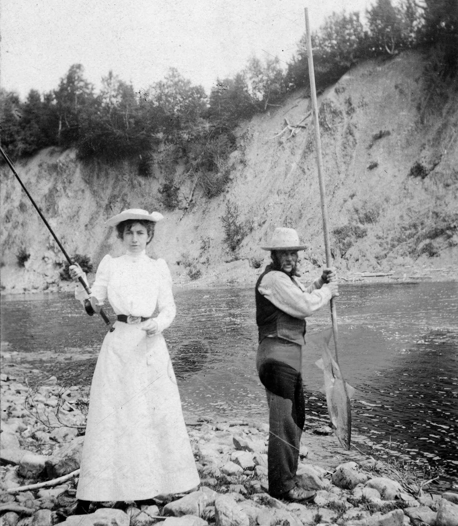 A slender woman with a fishing rod next to a guide holding a fishing net.