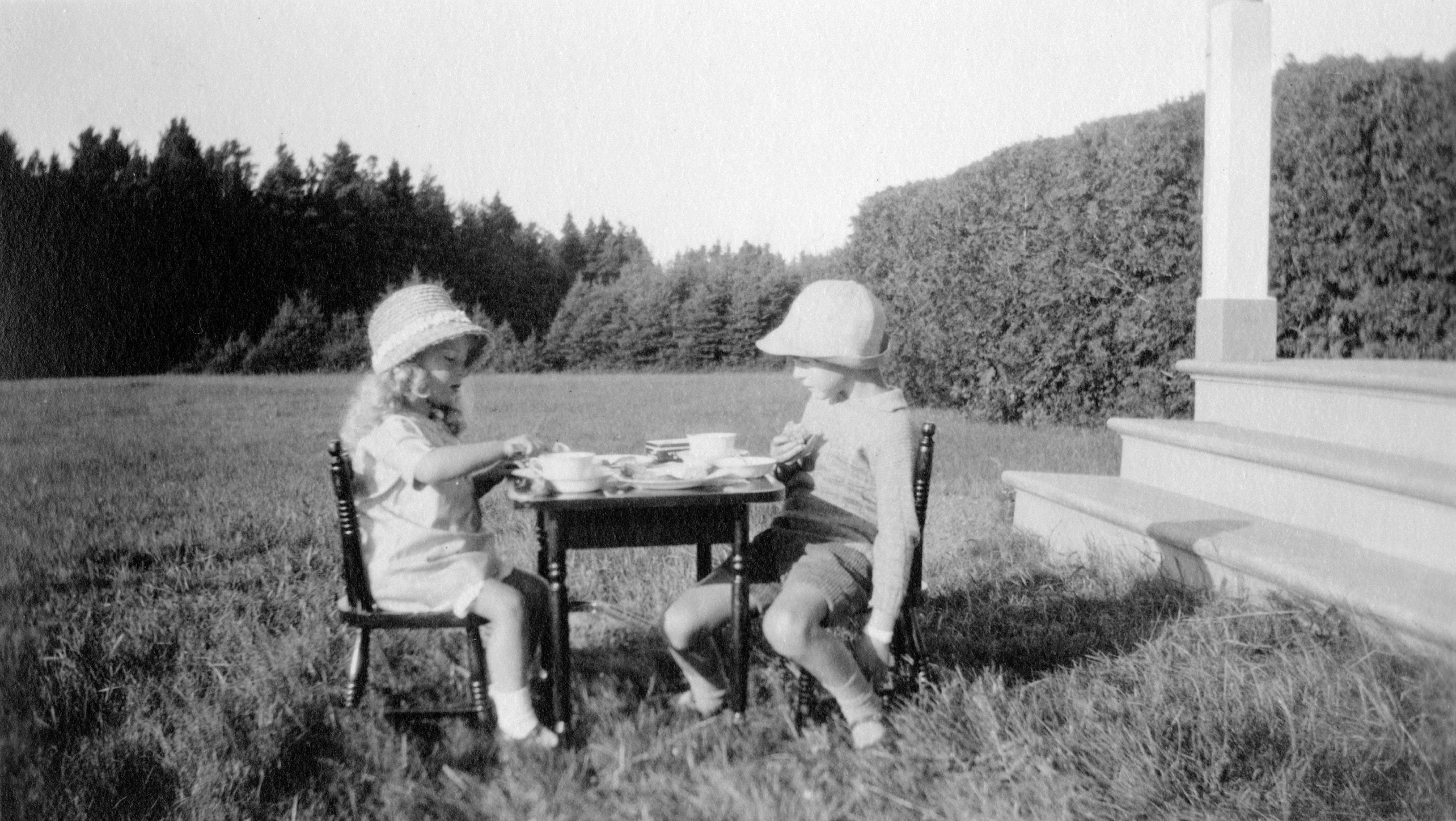 Deux enfants dégustent une collation posée sur une petite table installée à l'extérieur, sur la pelouse.