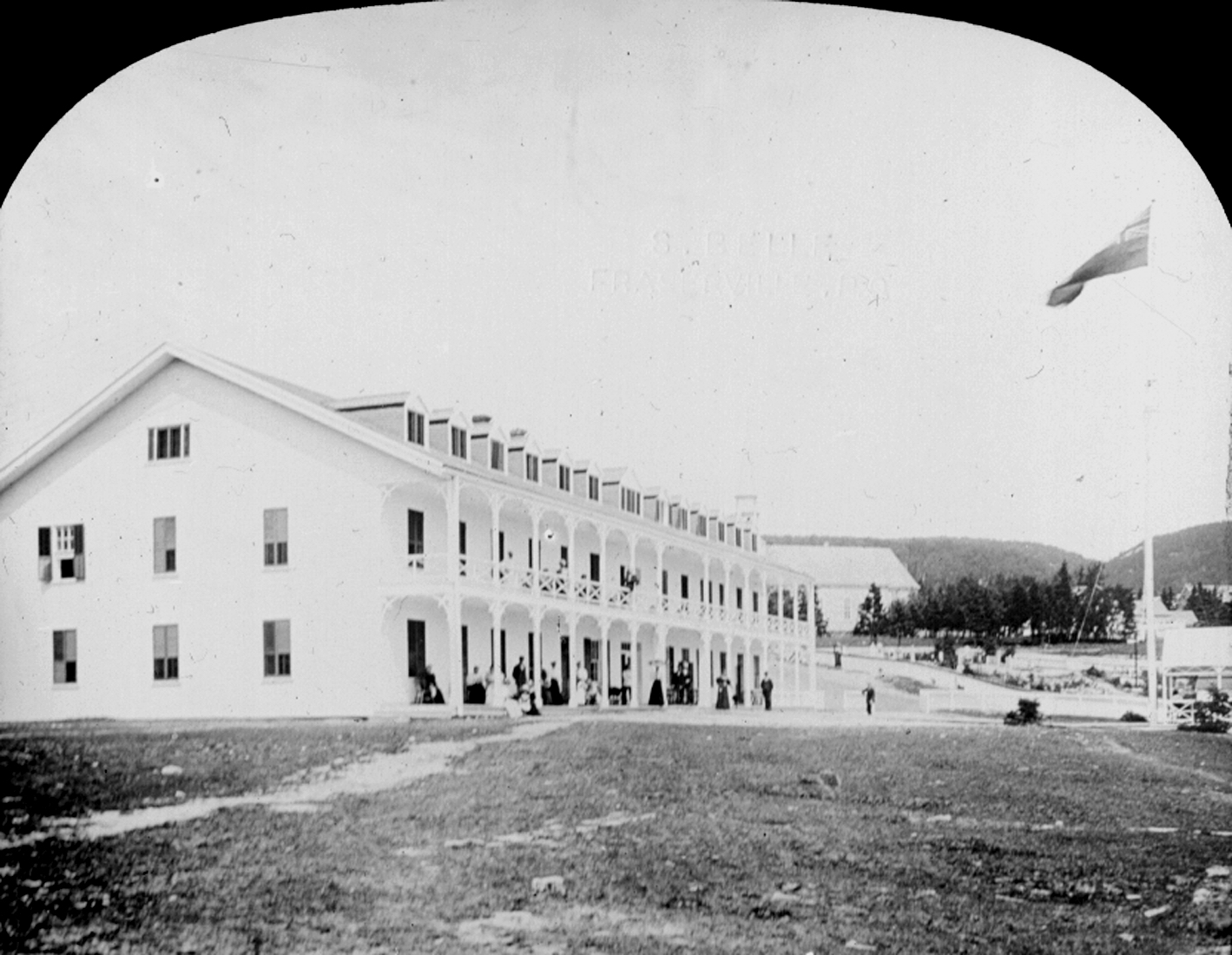 Photograph of a large hotel with very long galleries, on ground that has not been landscaped.