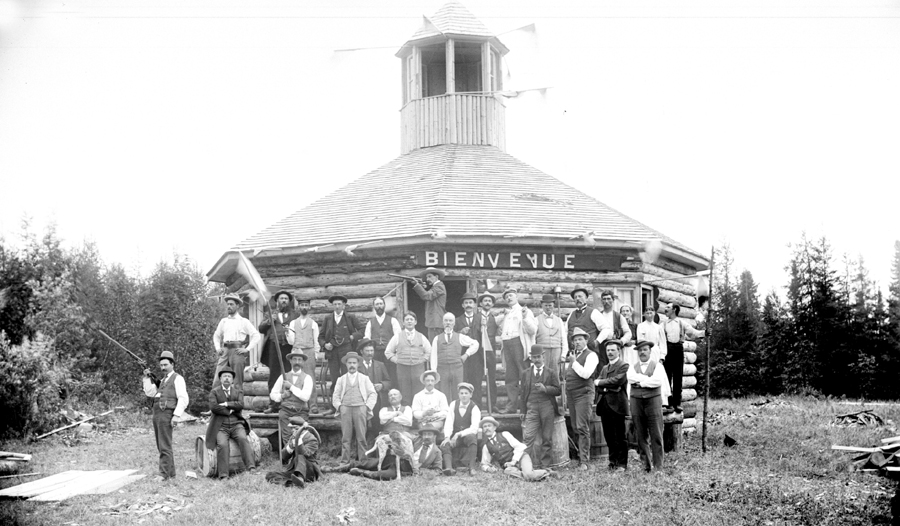 Men armed with rifles standing in front of an unusual log cabin.