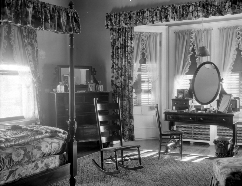 A dressing table and a canopy bed in a bedroom decorated with flowery drapes.