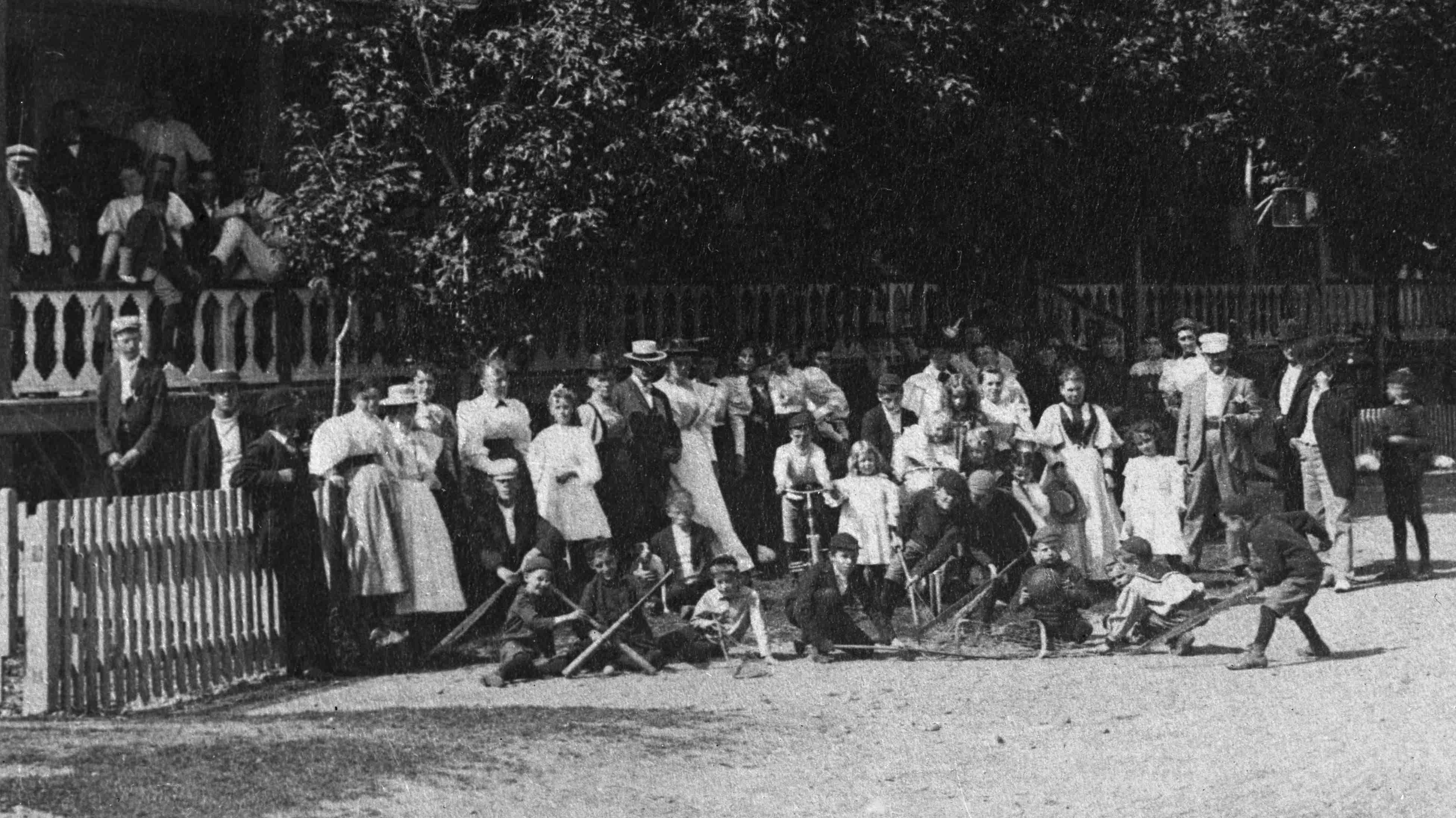 Group photograph in front of a large porch, with children showing off many pieces of sports equipment.