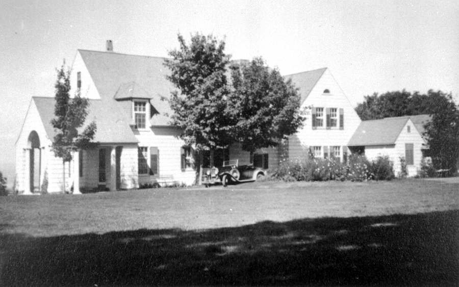 Une villa et son terrain. Une automobile ancienne est stationnée devant la maison.