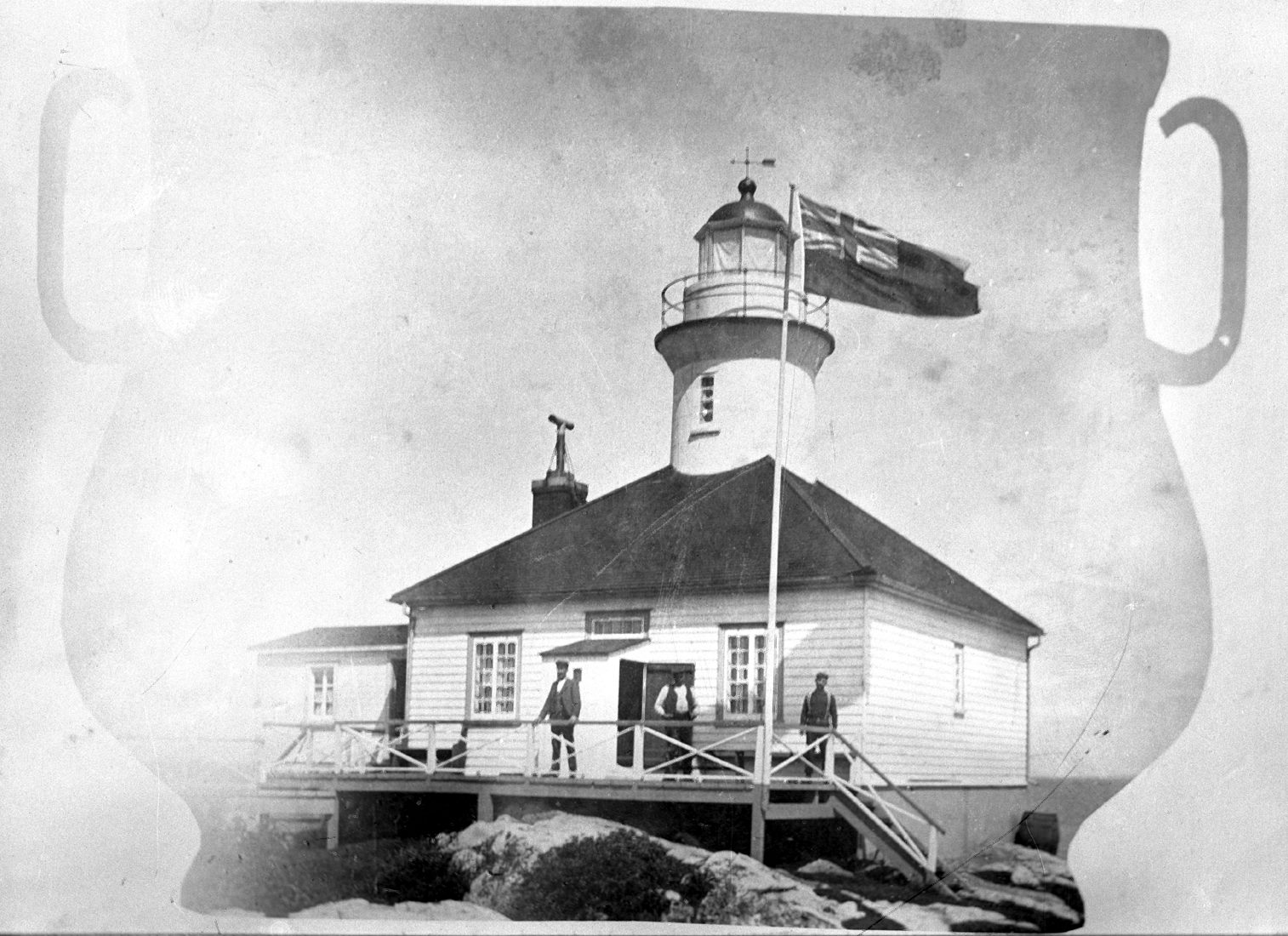 Three men pose in front of a lighthouse on the rocks. The picture is in the shape of an urn with two handles.