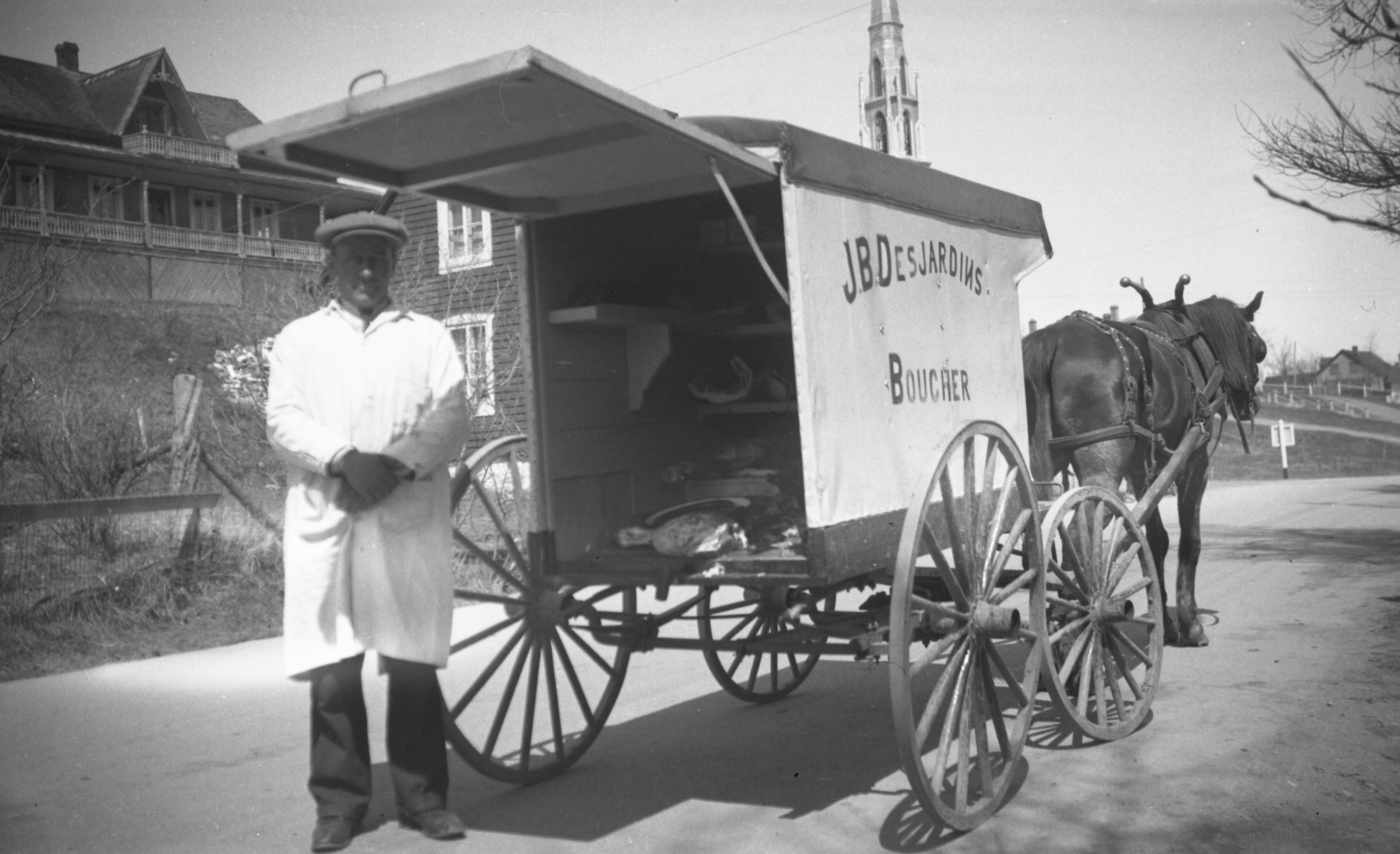 A butcher in a white smock poses in front of his horse-drawn four-wheeled delivery cart.