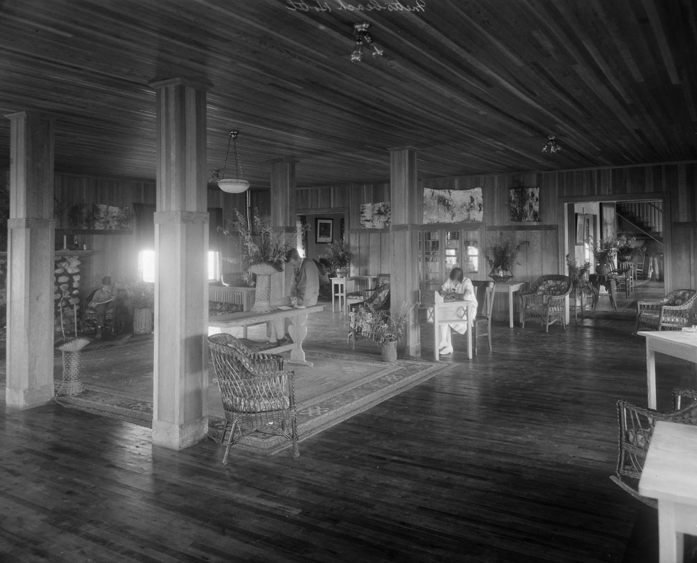 Three adults reading or writing in Boule Rock Hotel’sgreat sitting roomwith unpainted wood walls.