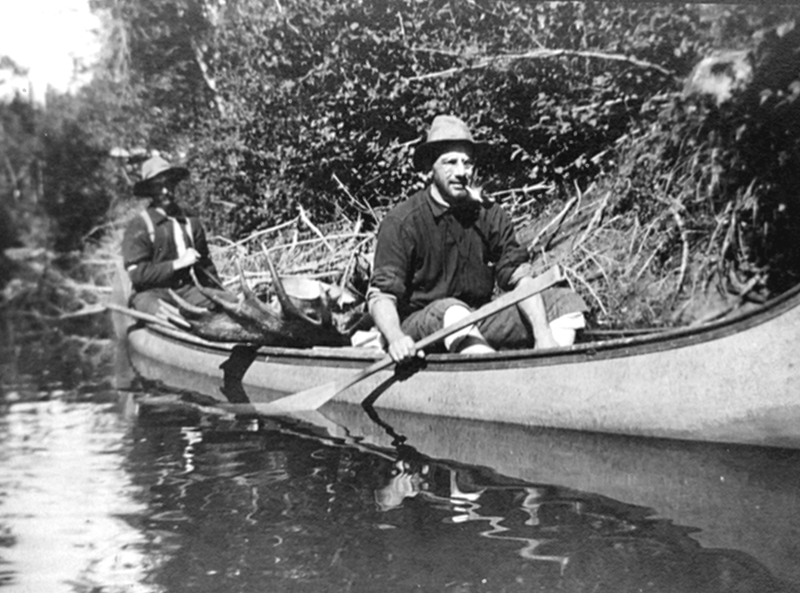 Two men in a canoe, carrying a moose.