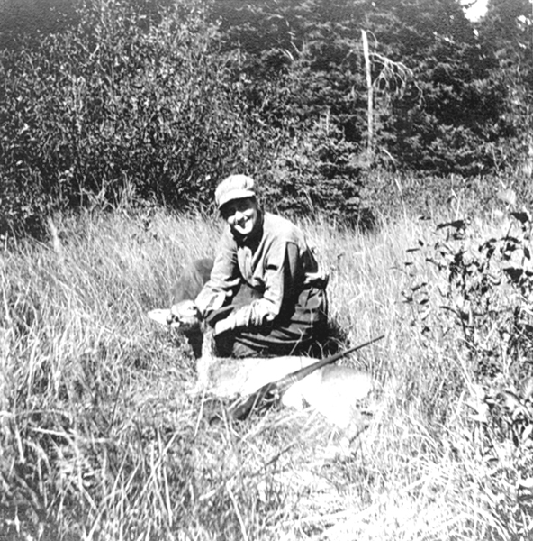 A woman kneeling in the grass, showing off her deer trophy.