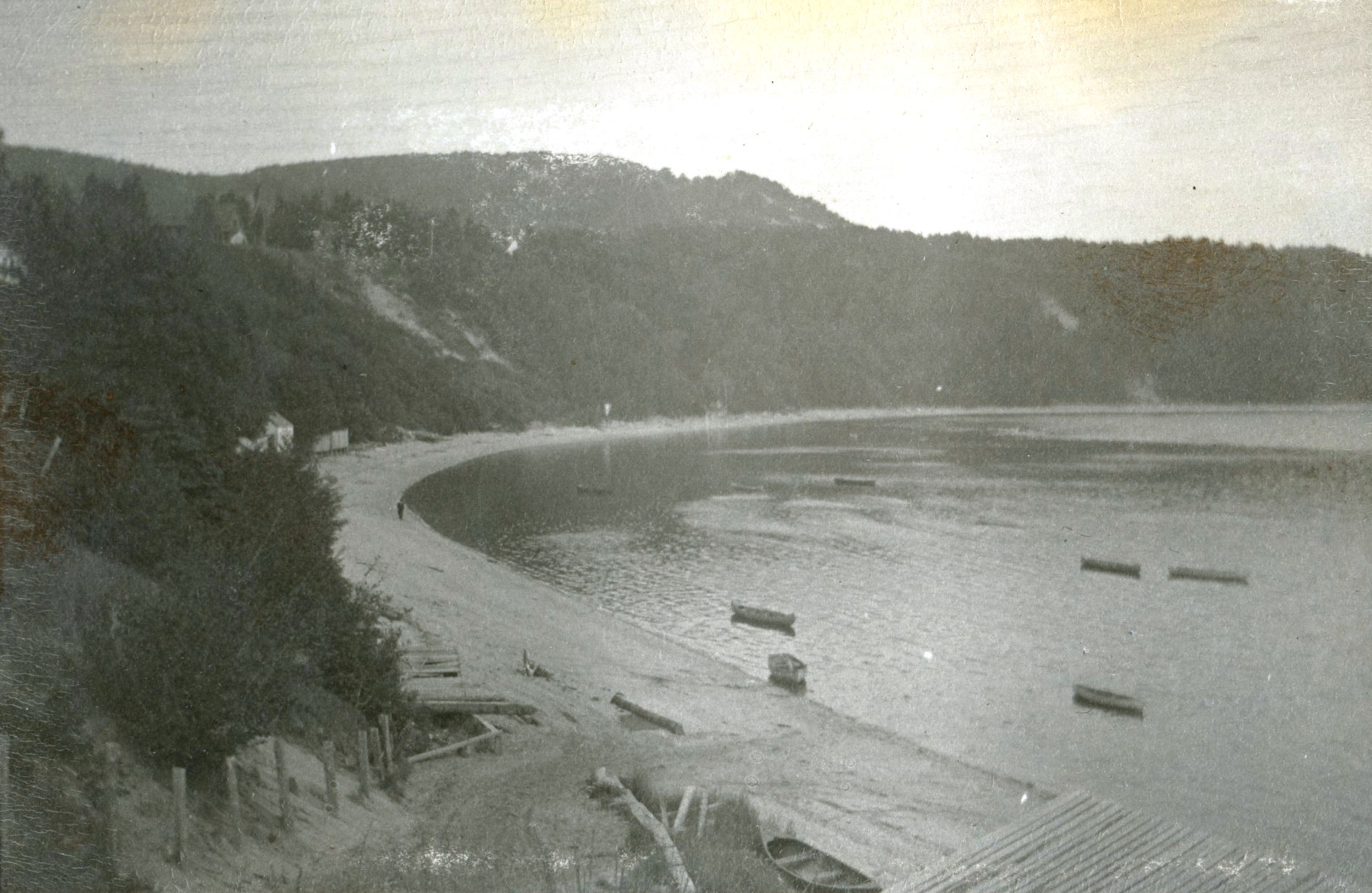 A beach and a cove at the foot of a cliff, with several canoes floating in the water.