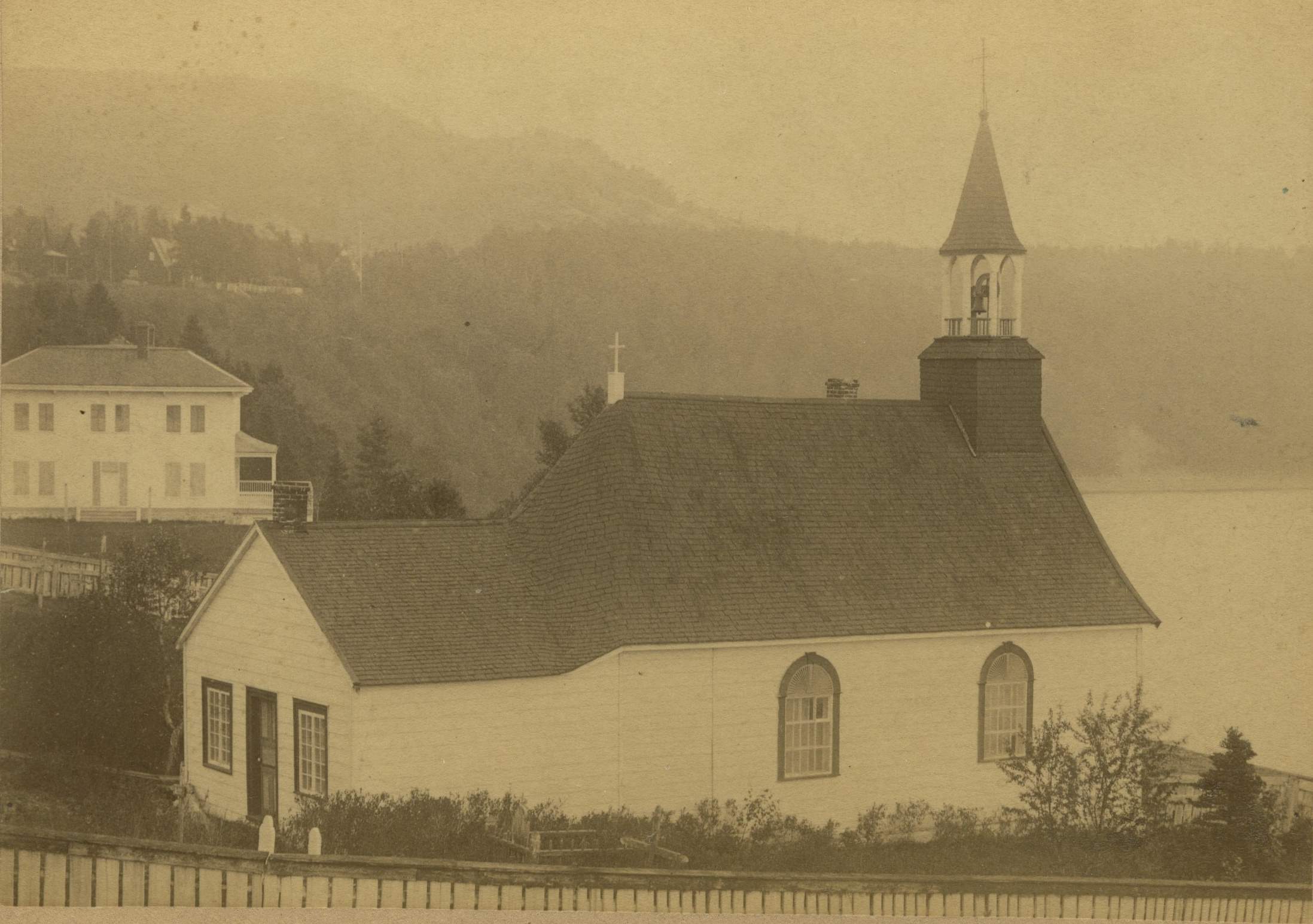 A chapel and large white house, on top of a cliff facing the river.