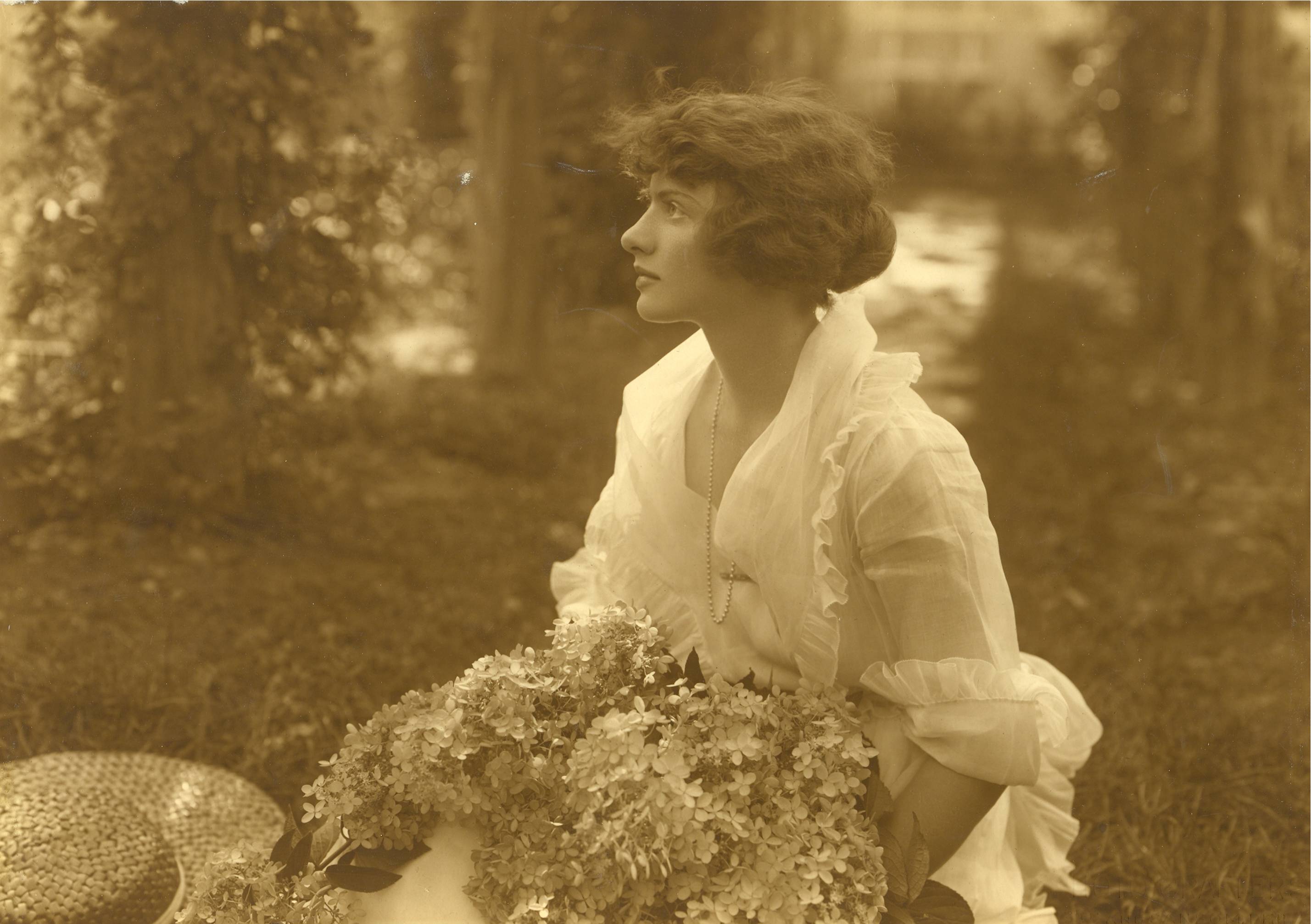A profile of young woman holding an enormous bouquet and wearing a light-weight white blouse.