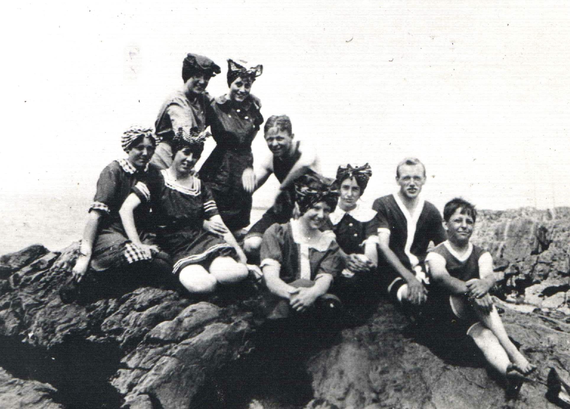 Neuf jeunes personnes posent sur un rocher au bord du fleuve, vêtus de maillots de bains du début du vingtième siècle.