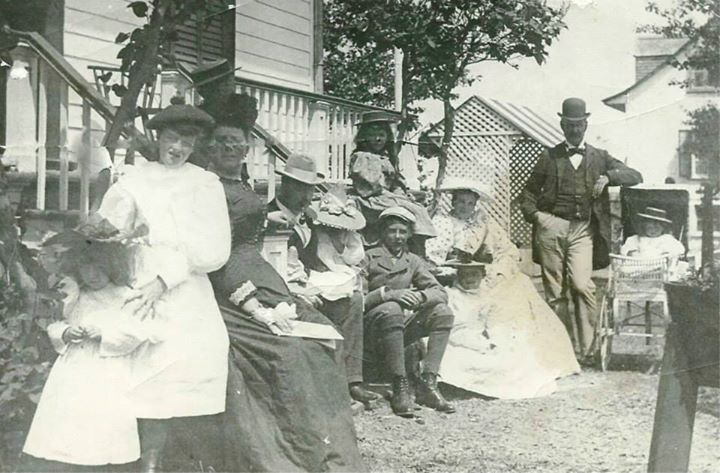 A black-and-white photograph shows a family of some ten well-dressed children and adults in front of a house.