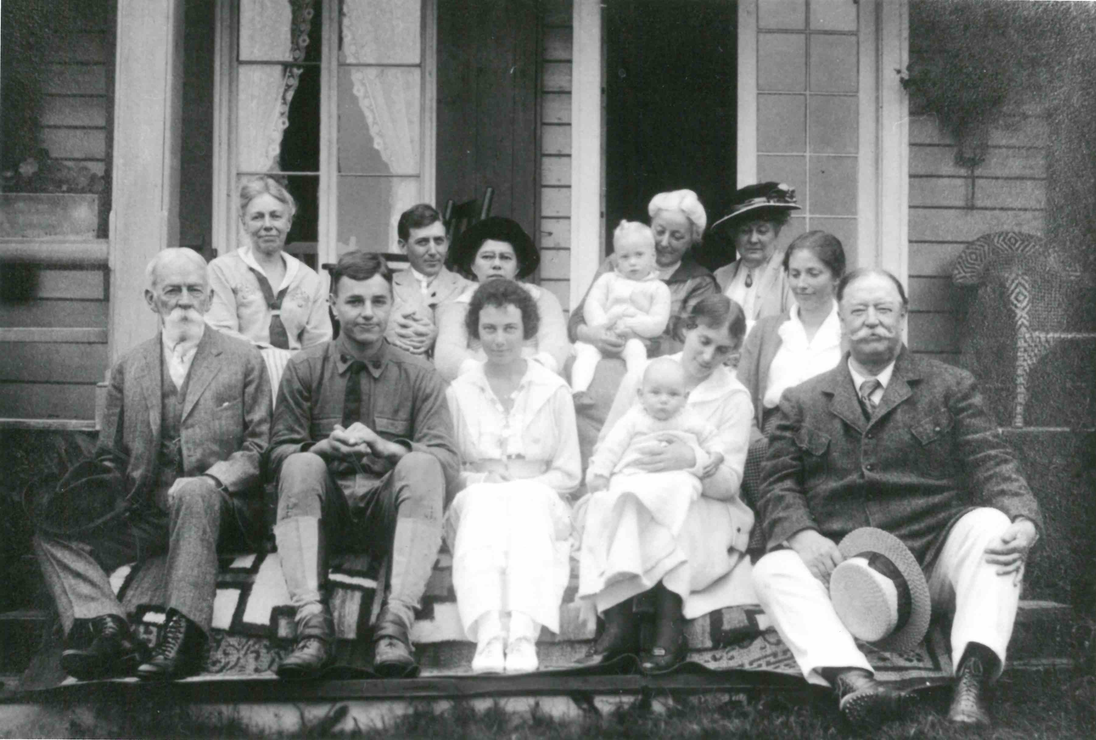 A dozen people of all ages posing for a family photograph on the steps of a summer home.