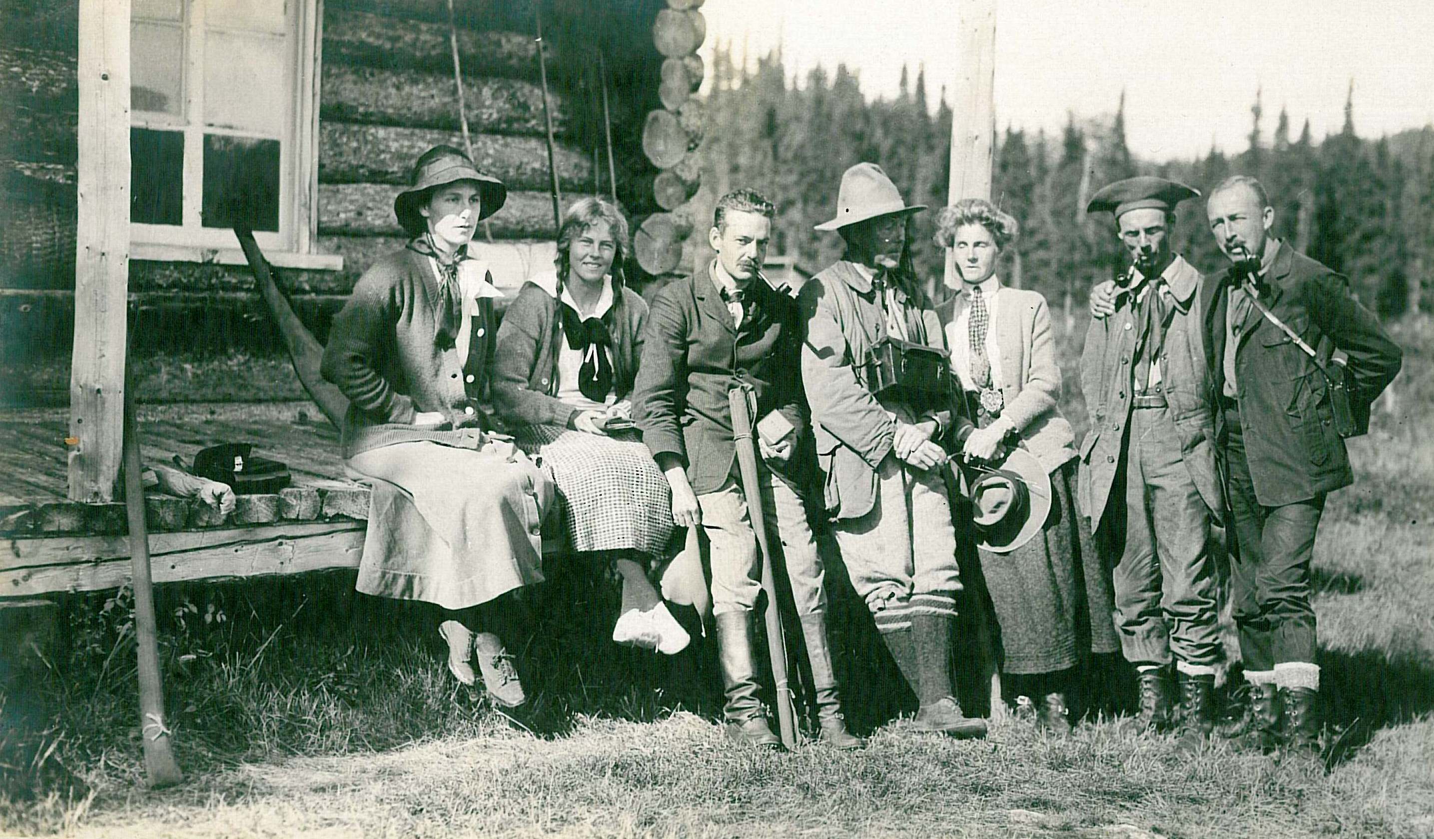 Quatre hommes et trois femmes posent devant un camp de chasse et pêche en rondins.