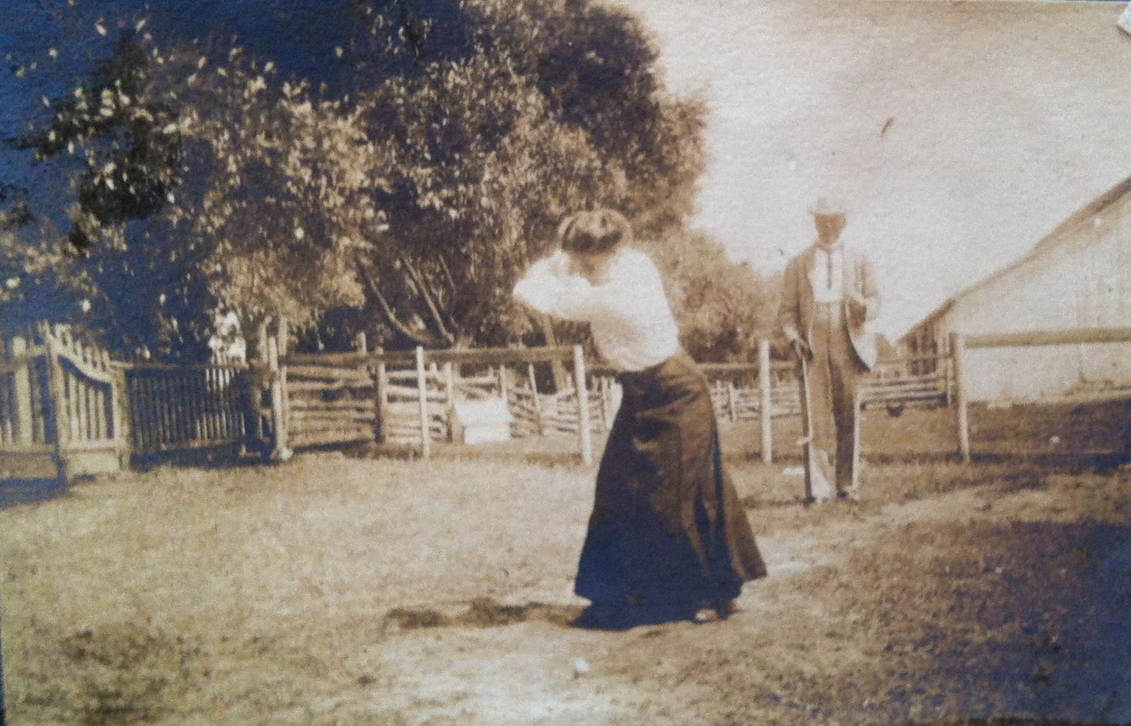 A woman swinging to hit a golf ball while a man waits in the background.