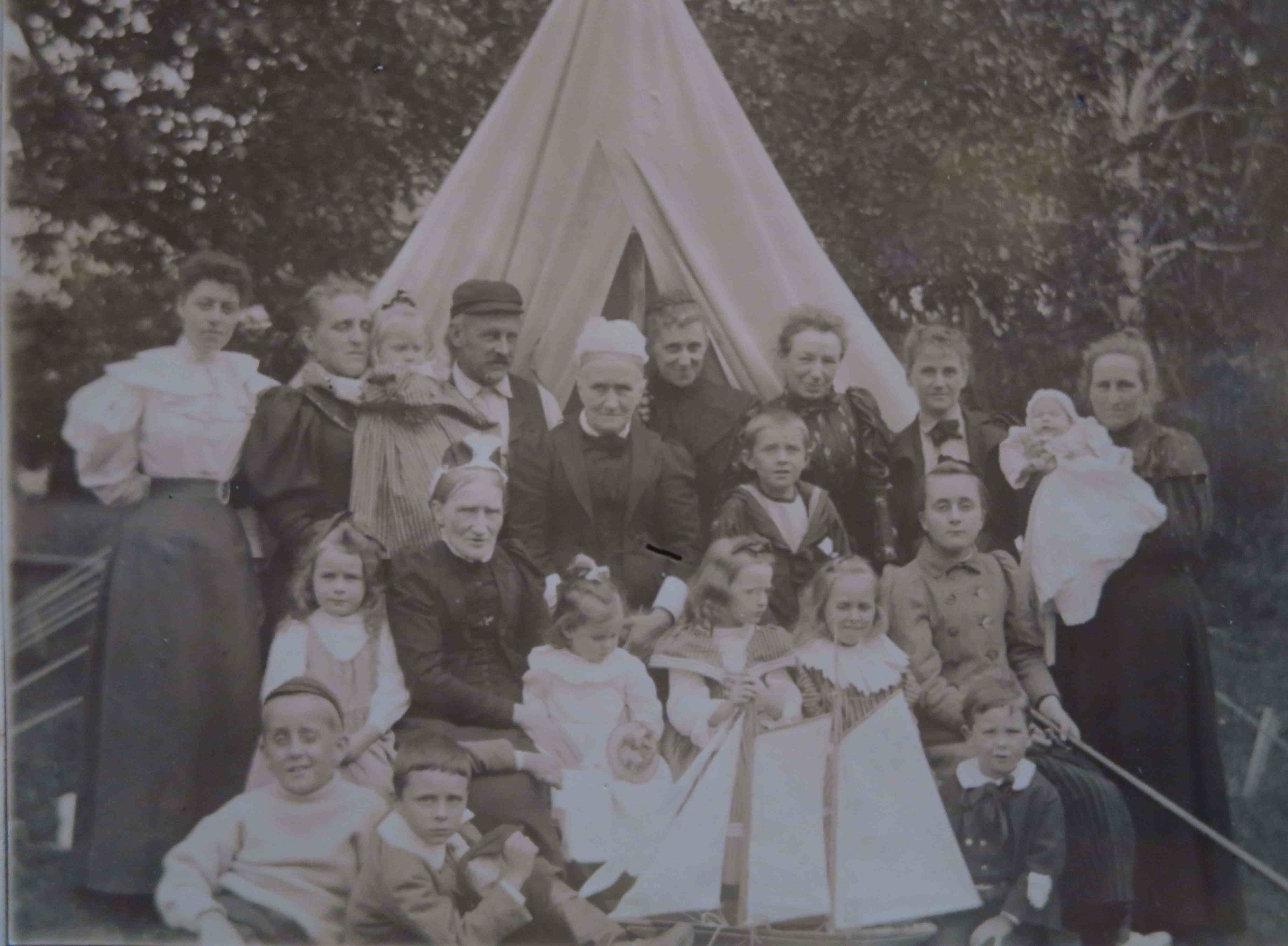 A black-and-white photo portrait of some twenty people of all ages in front of a tent.