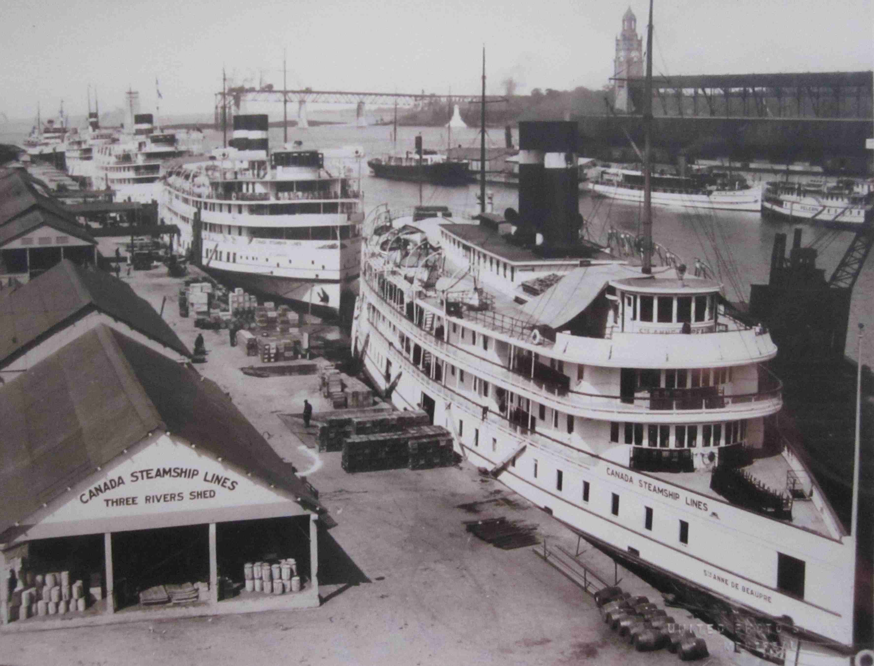 Photographie de grands navires de croisière à vapeur dans un port. En arrière-plan, on aperçoit un pont en construction.