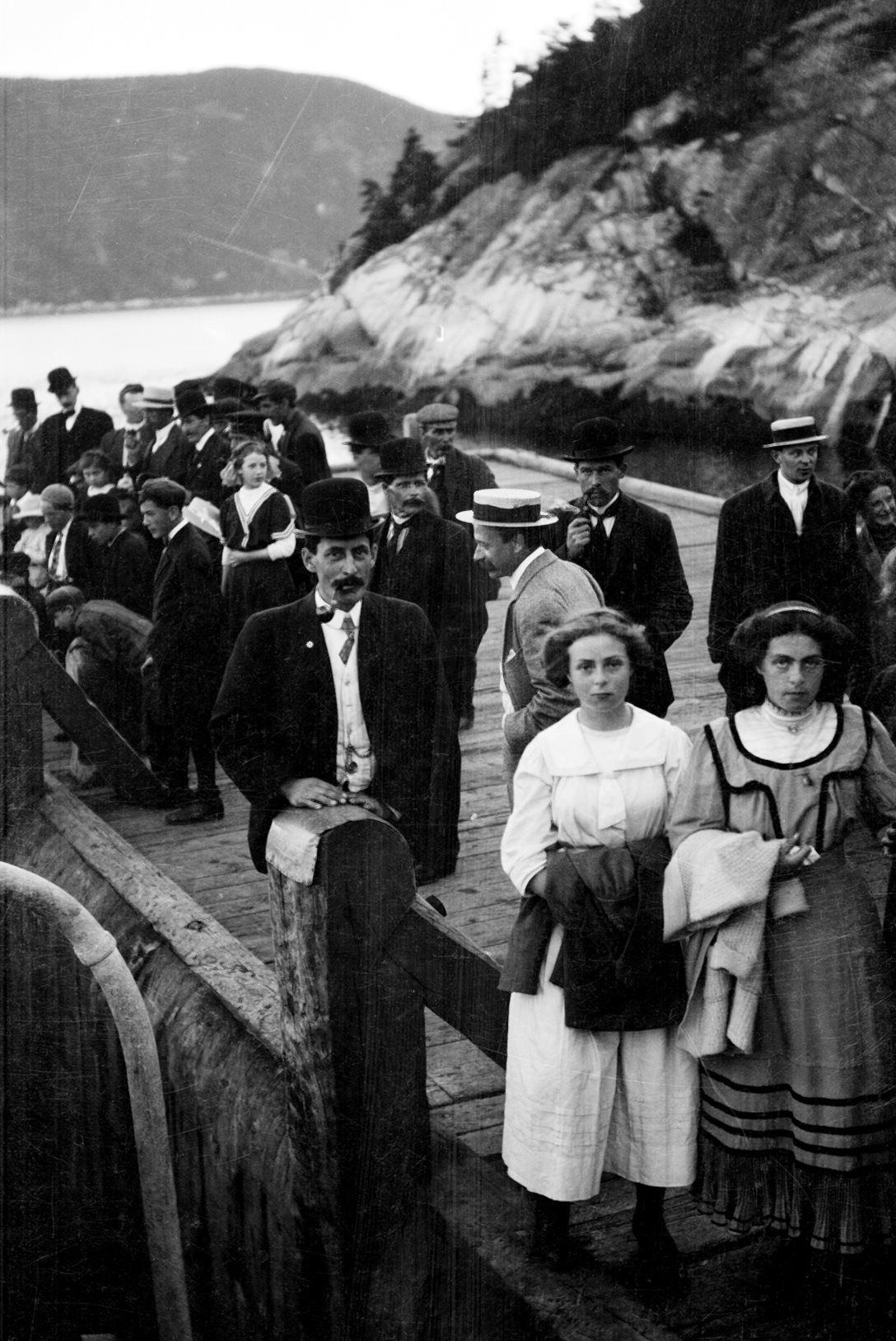 Des gens sur un quai, dans un paysage montagneux.