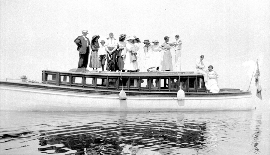 A dozen people posing on the roof of a motorized yacht.