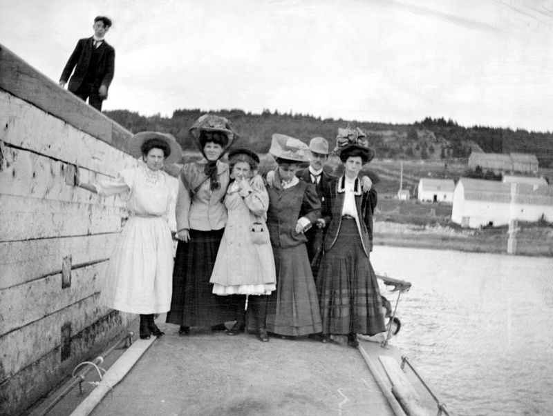 A group, mostly women wearing large hats, at the foot of a wharf.