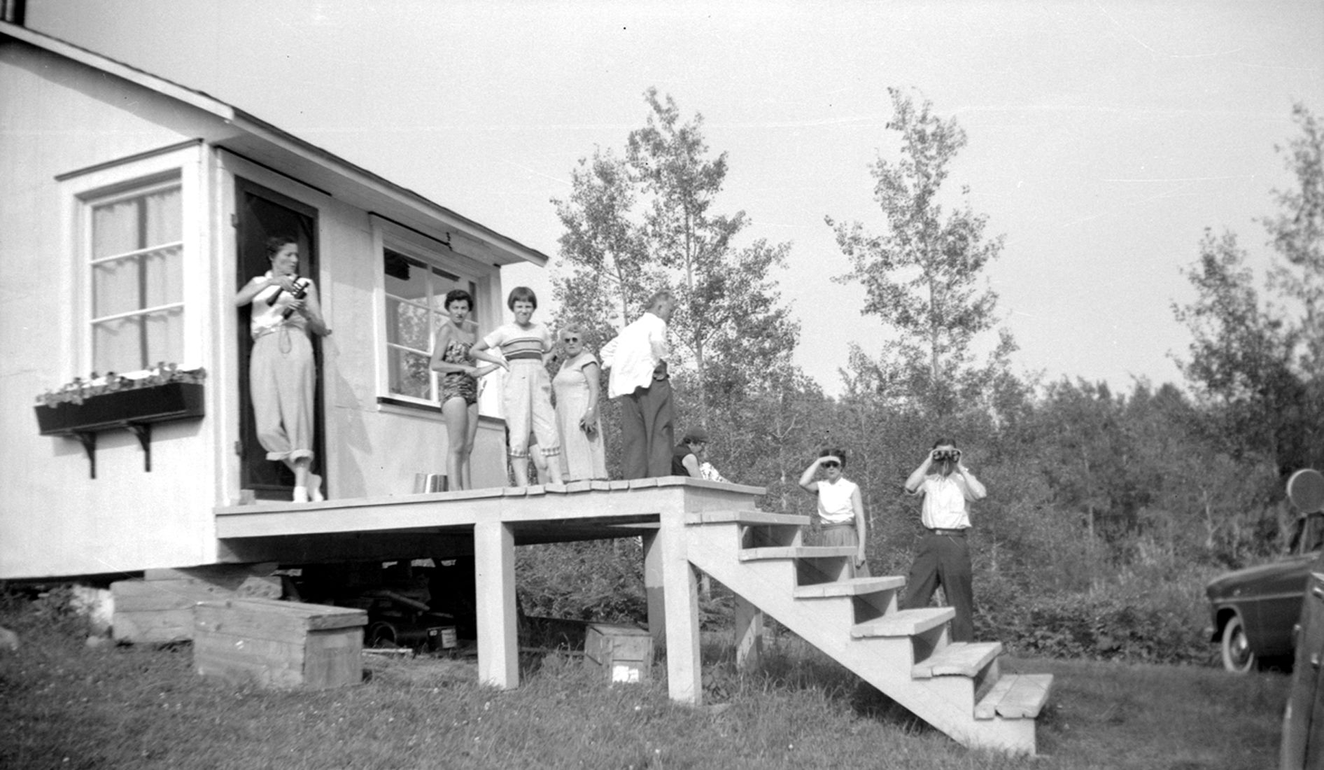 A dozen or so people behind a cottage in casual dress, two holding binoculars.