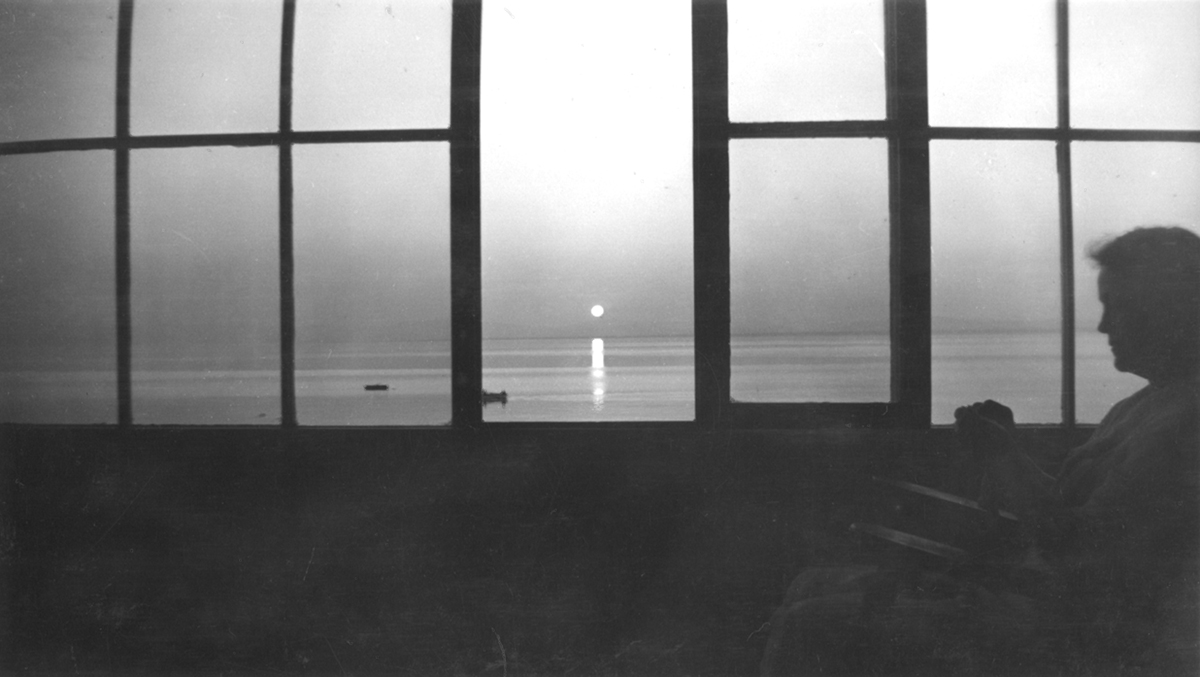 Une vieille dame assise à la fenêtre regarde le soleil se coucher sur le fleuve Saint-Laurent.