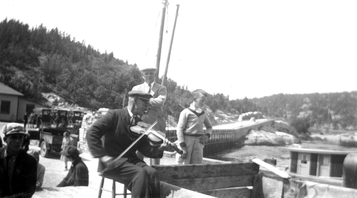 An old man playing fiddle on a wharf.