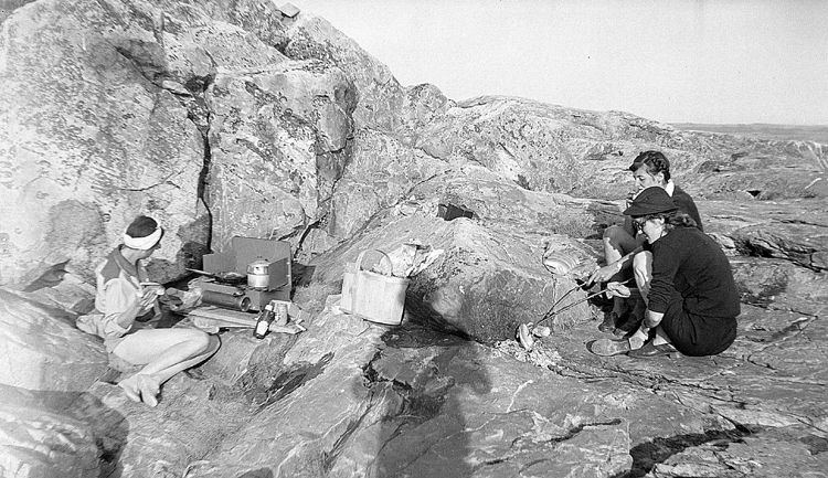 Young women cooking hotdogs on a rock.