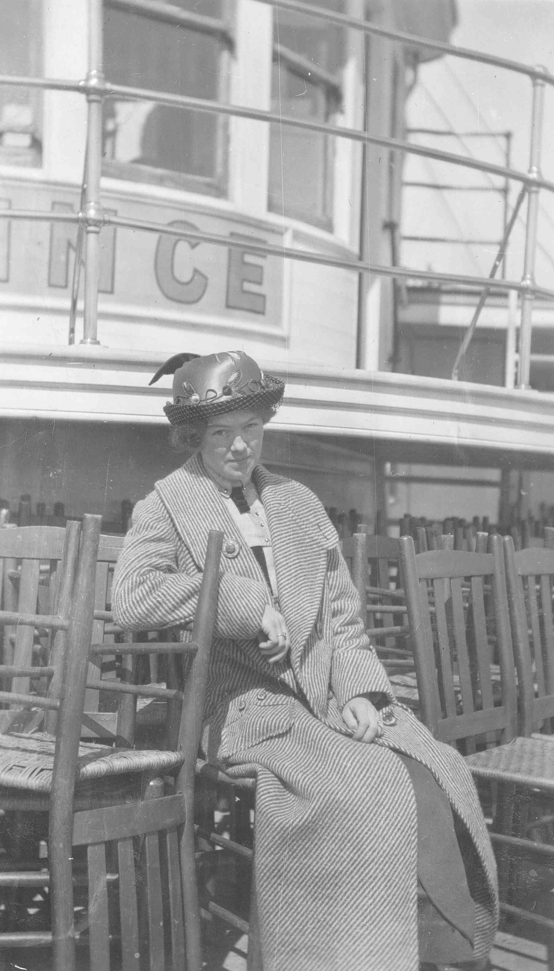 Une jeune femme est assise sur le pont d’un navire, entourée de chaises empilées.