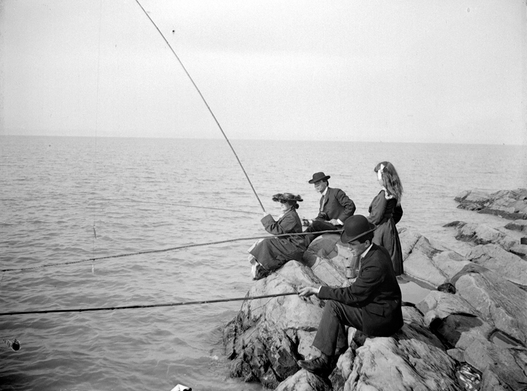 Deux hommes et deux femmes pêchent le poisson, assis sur des rochers.