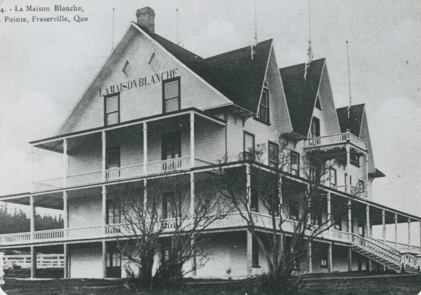 A large building with wood siding, surrounded by verandas and dormer windows.