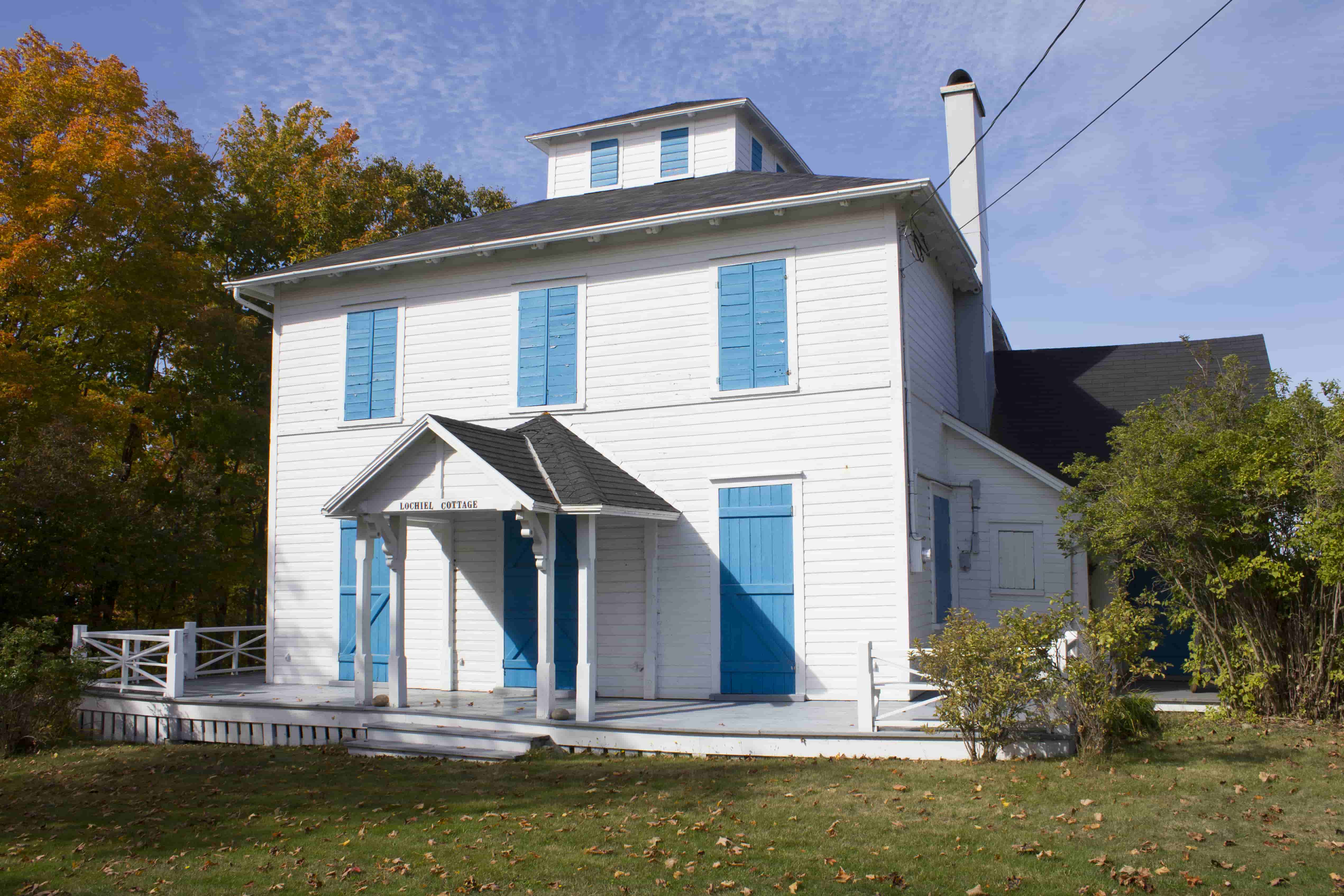 A large white house with closed blue shutters.