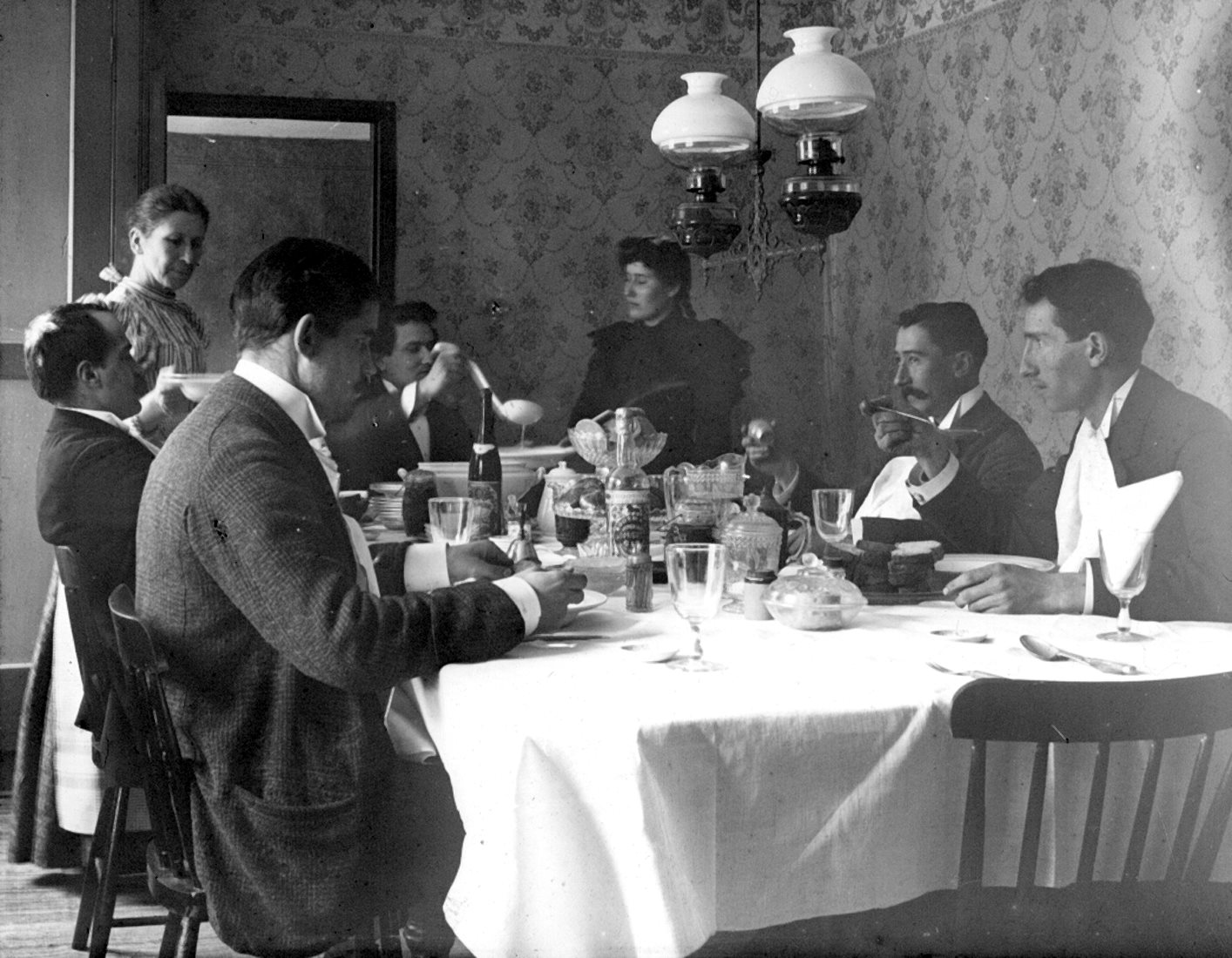 A group sitting at a well-garnished table, with a woman serving the meal.