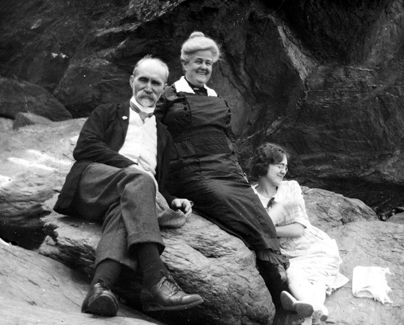 A rather distinguished older couple and a young woman sitting on a rock, relaxed and smiling.