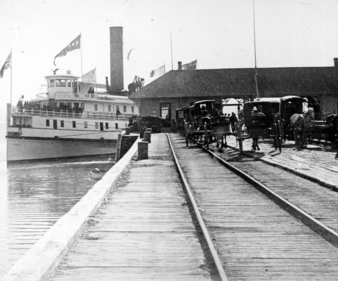 A steamboat at a wharf equipped with rails and porters waiting for passengers to land.