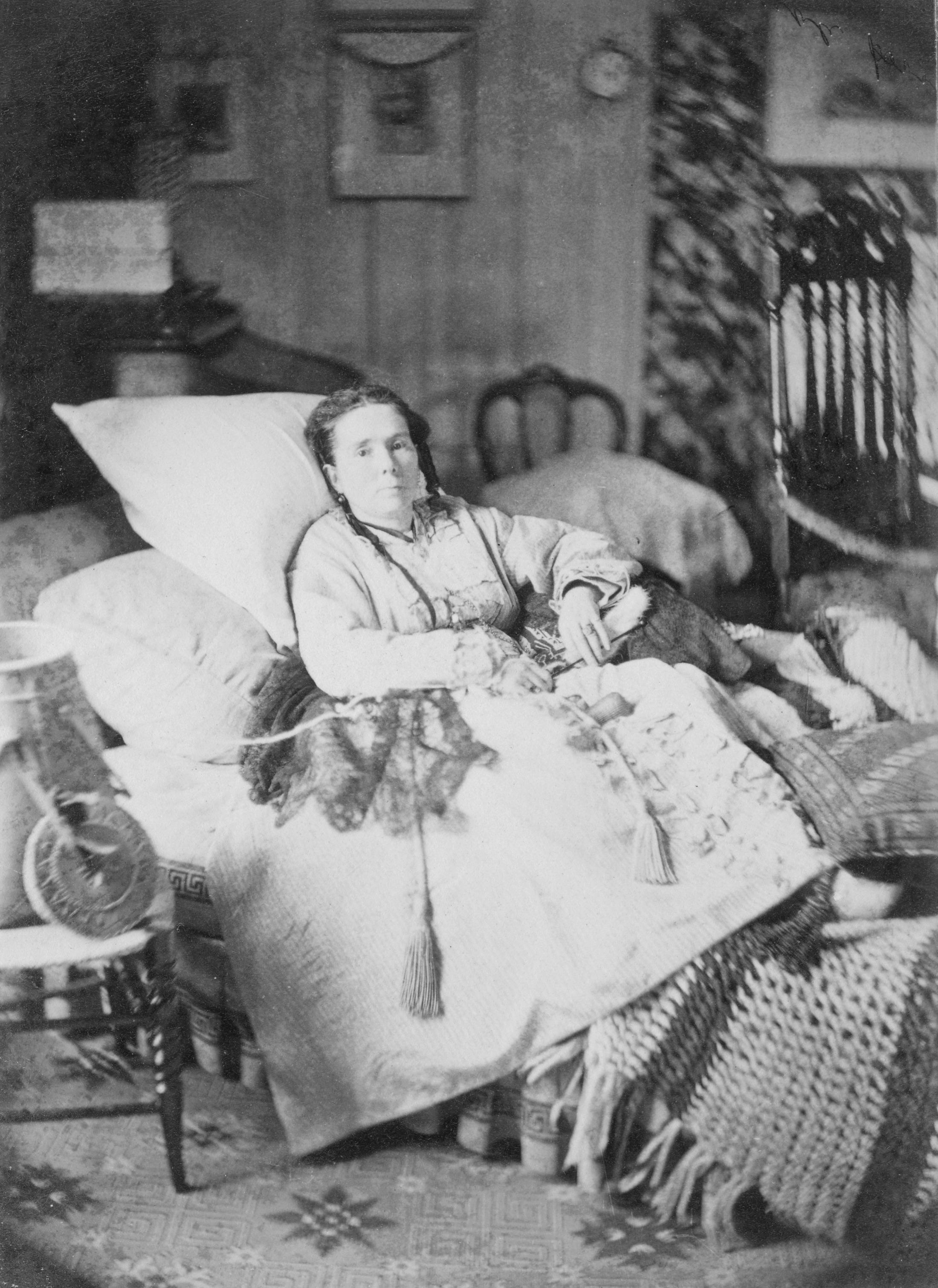 Photographie en noir et blanc d’une femme malade qui se repose dans un lit très confortable.