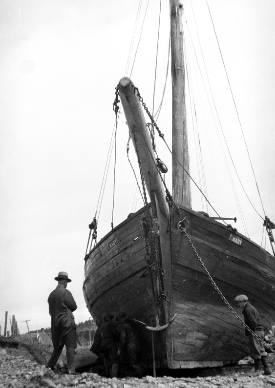 Two men observing a schooner on the shore.