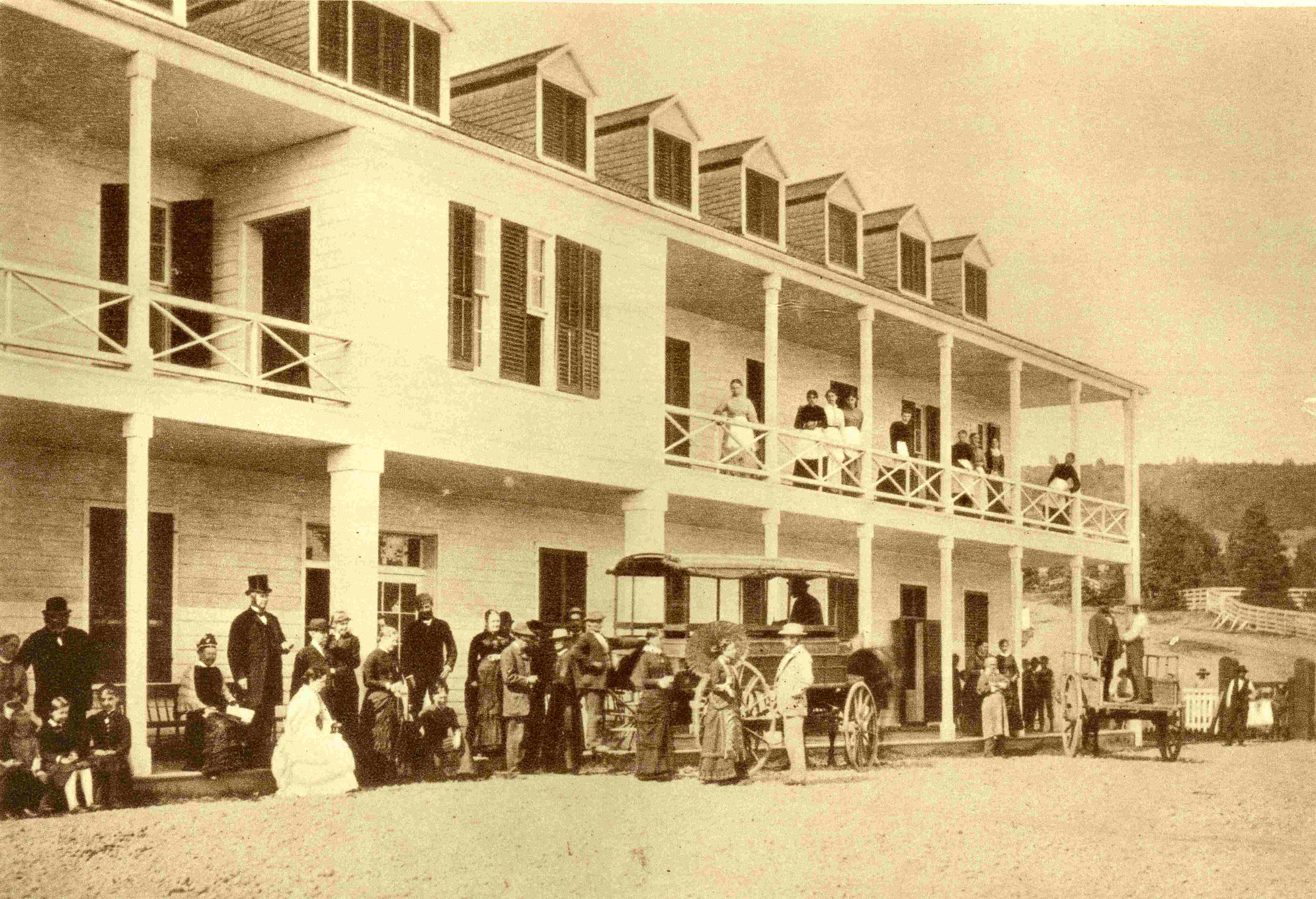 Clients milling in front of a hotel and a horse-drawn omnibus for transporting passengers.