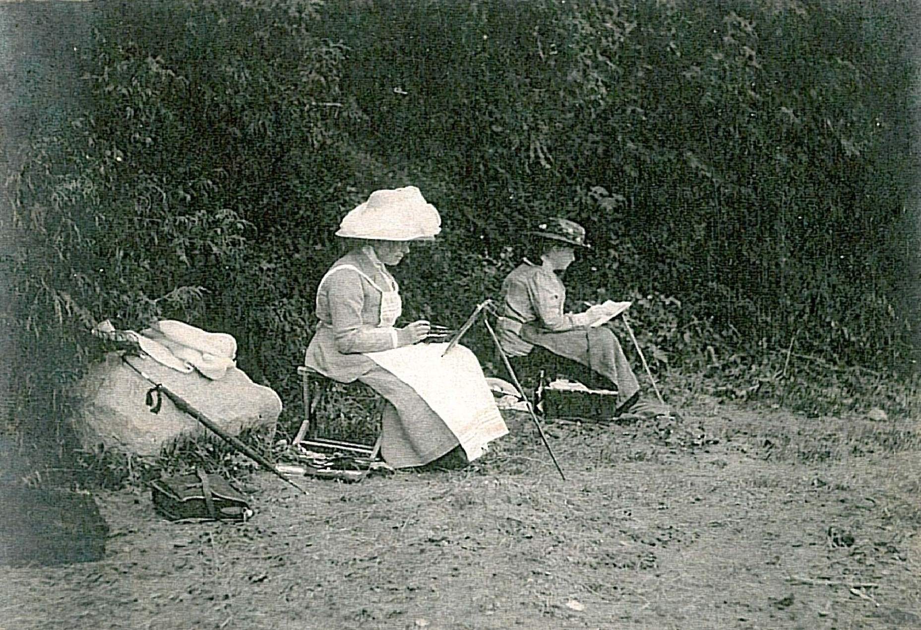 Two women painting on a beach, canvases on portable easels.