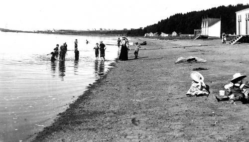 Des femmes et des enfants profitent de la plage. Deux enfants jouent dans le sable. Les baigneurs portent des maillots longs.