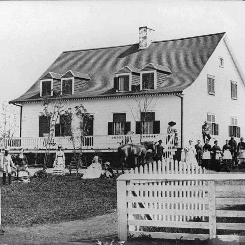A group of fifteen people posing in front of an old country home.