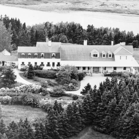 Imposante villa bordée d’arbres avec un aménagement paysager soigné, située sur un point élevé près d’une rivière.