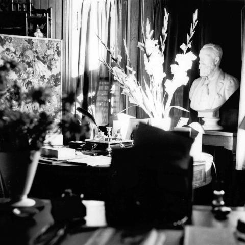 A black and white photograph of an office heavily decorated with knickknacks and flowers.