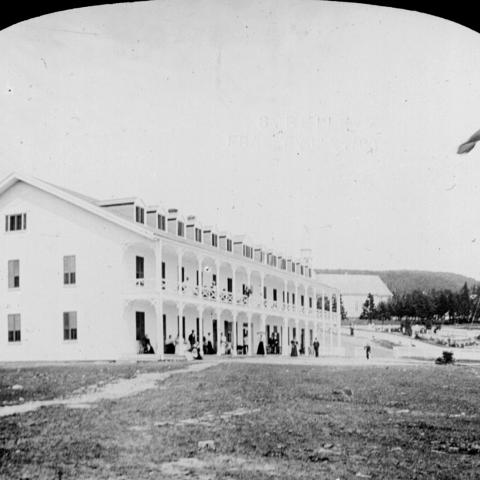Photograph of a large hotel with very long galleries, on ground that has not been landscaped.