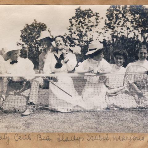 Tennis players in dresses, jackets and shirts sitting near the net.