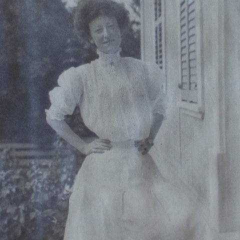 A woman wearing a long white dress with a high neckline; she is quite petite.