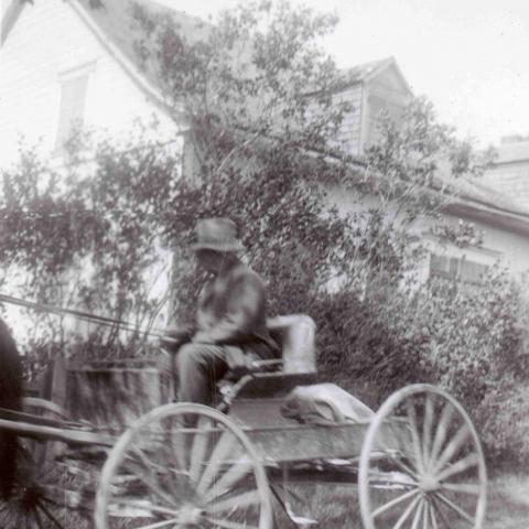 man drives a rustic four-wheeled horse-drawn carriage.