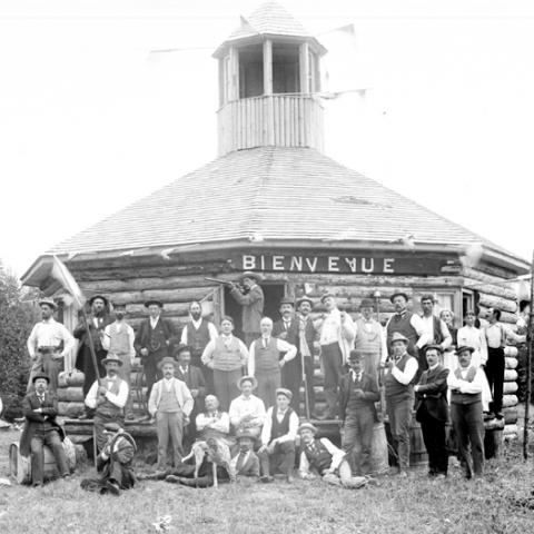 Men armed with rifles standing in front of an unusual log cabin.